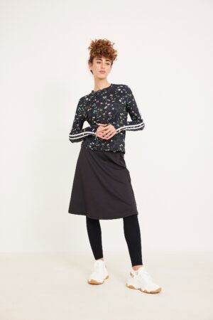 שמלת ספורט שחורה עם פרחים צבעוניים ועליונית שחורה עם פסים לבנים, נעלי ספורט לבנות, אופנה נוחה וסטיילורית.