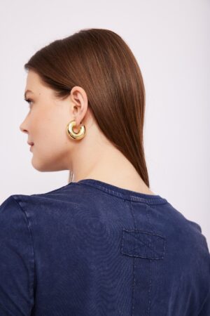 תמונה של אשה עם תכשיט עגיל זהב גדול, מצולמת בפרופיל עם שיער חום אדמוני ושילוב עם בגד דנים כהה.